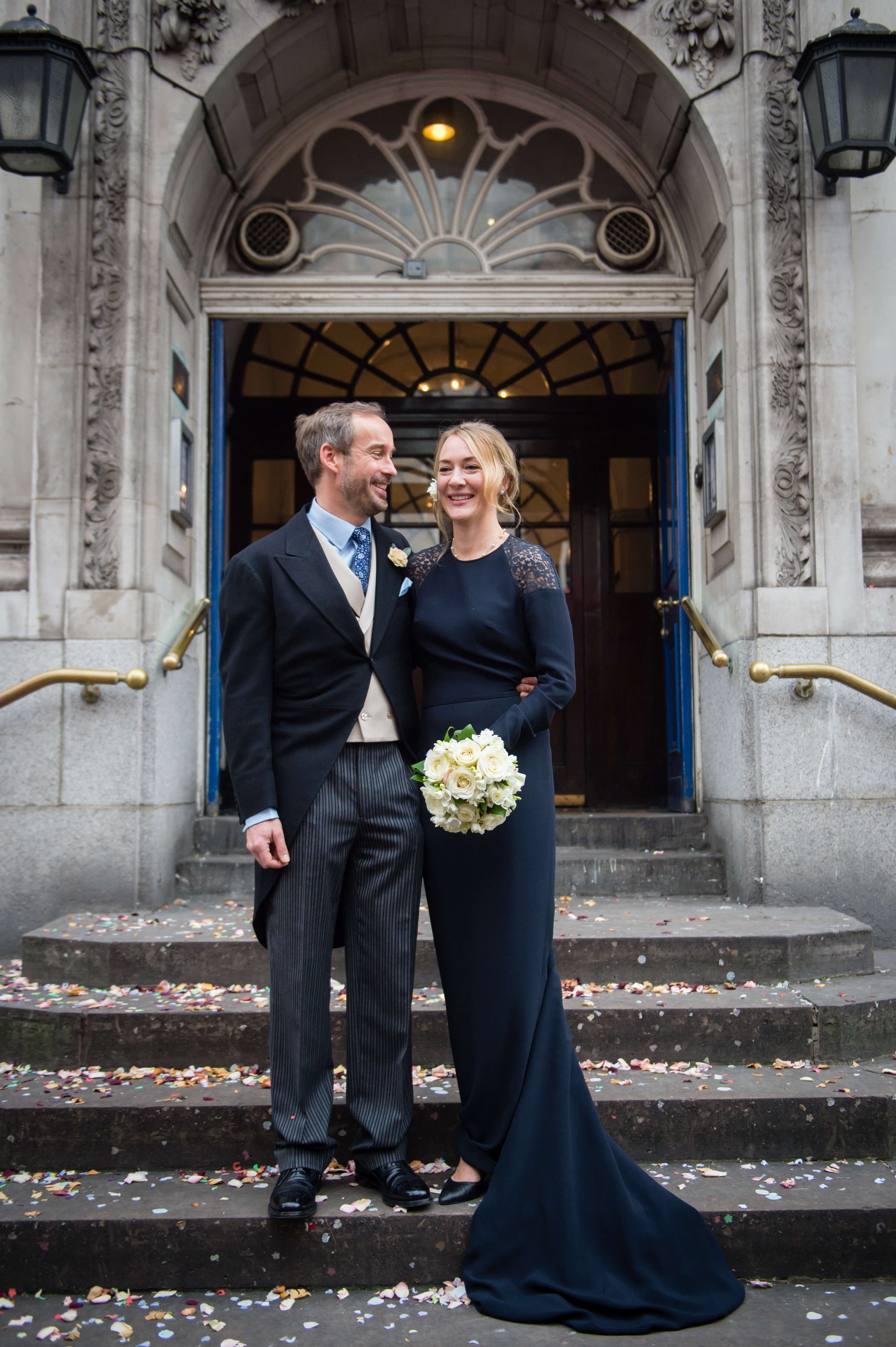 bride and groom on the steps at chelsea old town hall wearing stella mccartney navy silk wedding gown